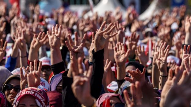 People cheer and flash a four finger sign called 'the rabia sign' as the Turkish president delivers a speech in Istanbul, on April 15, 2017, during a rally on the eve of the constitutional referendum