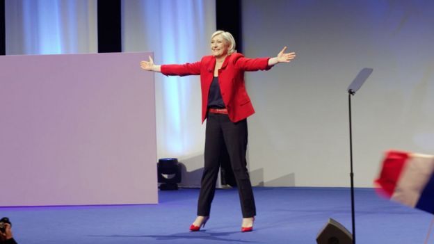 Marine Le Pen abriendo los brazos hacia el público en una presentación.