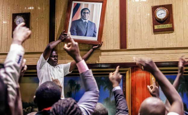 People remove, from the wall at the International Conference centre, where parliament had their sitting, the portrait of former Zimbabwean President Robert Mugabe after his resignation on November 21, 2017 in Harare.