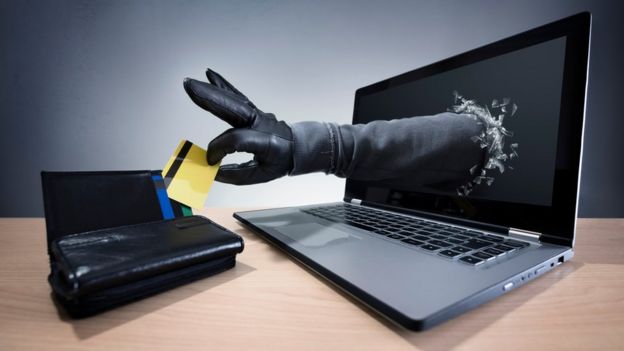 Una mano con guante sale de una pantalla de computadora para robar una tarjeta de crédito.