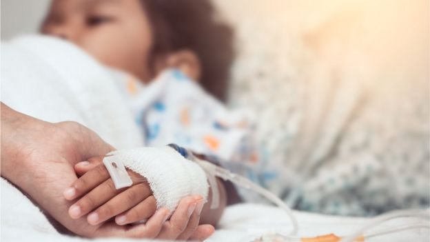 Mão de adulto segura a mão de uma criança hospitalizada