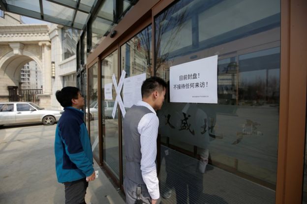 People look through the windows of a sales office of a property, with a paper on the window reading