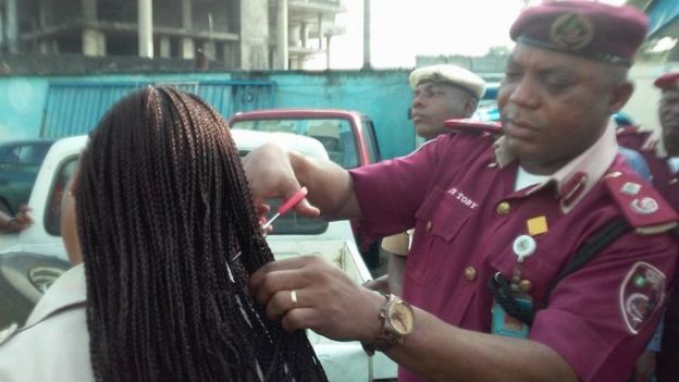 Man wearing a maroon beret and uniform takes scissors to a female employee's hair