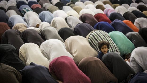 A young boy pops his head up as other Muslim men bend down to pray