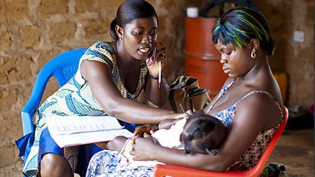 Health worker on the phone while she helps woman and baby