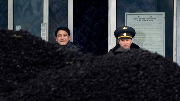 This file picture taken on 14 December 2012 from China's north-eastern city of Dandong, looking across the border, shows a North Korean military officer (R) and a North Korea man (L) standing behind a pile of coal along the banks of the Yalu River in the northeast of the North Korean border town of Siniuju