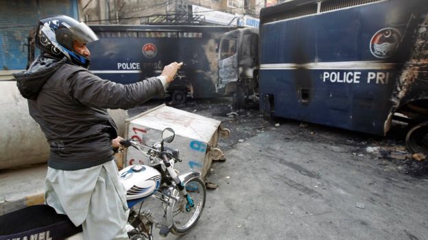 A man in Islamabad takes a photo of burnt-out police vehicles