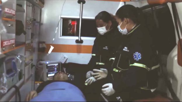Escena de aviso en el que se ve el interior de una ambulancia, con el paciente en la camilla, acompañado por dos paramédicas.