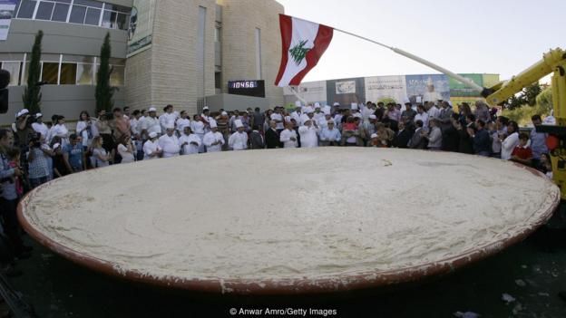 gente conglomerada ante un gigantesco plato de humus.