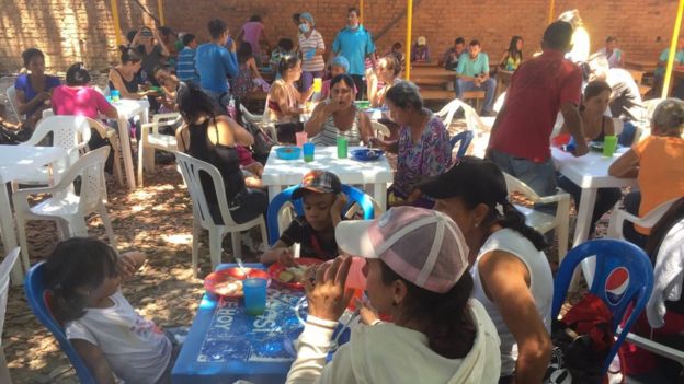 People sit at plastic tables and eat in the courtyard of a church in Cúcuta
