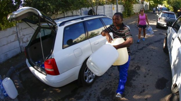 Un hombre lleva botellas de plástico para recoger agua en un manantial de Ciudad del Cabo.