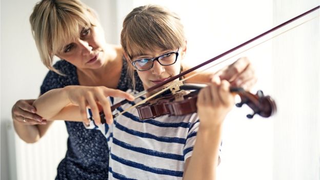 Mujer enseñando a niña a tocar violín.