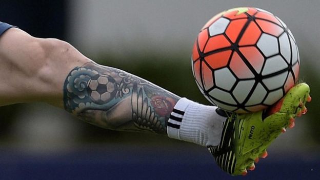 La pierna tatuada de un hombre, balanceando un balón