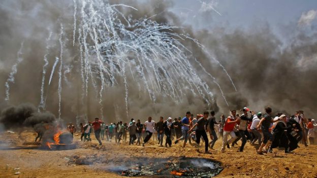 Palestinians run for cover from tear gas during clashes with Israeli security forces near the border between Israel and the Gaza Strip, east of Jabalia on May 14, 2018, as Palestinians protest over the inauguration of the US embassy following its controversial move to Jerusalem
