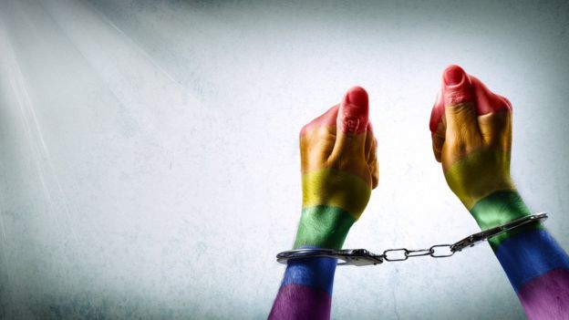 Un par de manos esposadas pintadas con los colores de la bandera gay