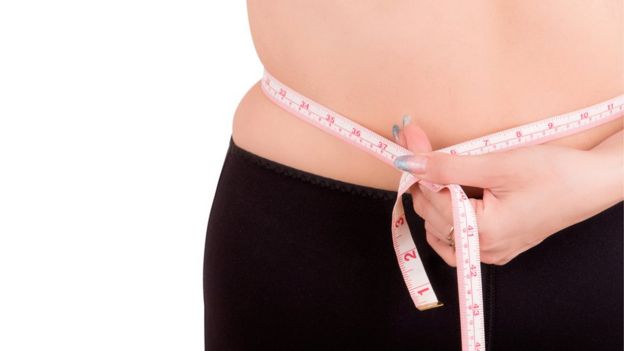Mujer se mide el abdomen con un centímetro.