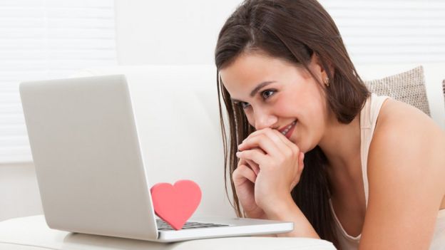 Una muchacha mira una laptop sonriente y abajo hay un corazoncito de cartón.