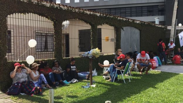 Manifestantes pró-Lula sentados no gramado de uma casa vizinha à PF de Curitiba
