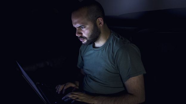رجل يجلس أمام كمبيوتر ليلا