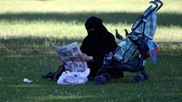 De niqab, mulher lê jornal em parque em Londres