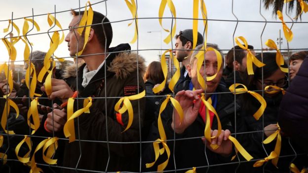 People tie yellow ribbons to a fence, as they protest in front of Germany's consulate after former president Carles Puigdemont