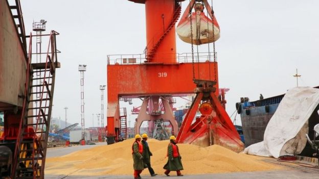 Workers walk past imported soybeans at a port in Nantong in China"s eastern Jiangsu province on April 4, 2018