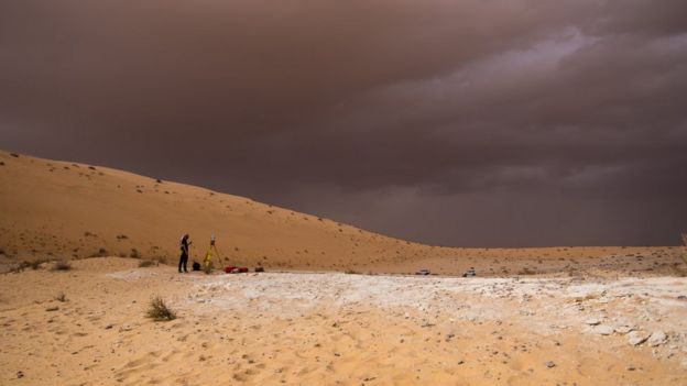 Un desierto y el cielo gris. Un científico de pie.