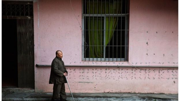 Elderly blind Chinese man walks past a building
