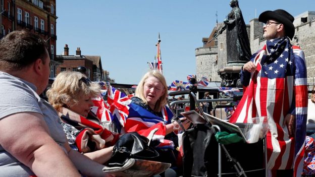 Tourists hold Union flags whilst draped in Union and US flags near Windsor Castle in Windsor