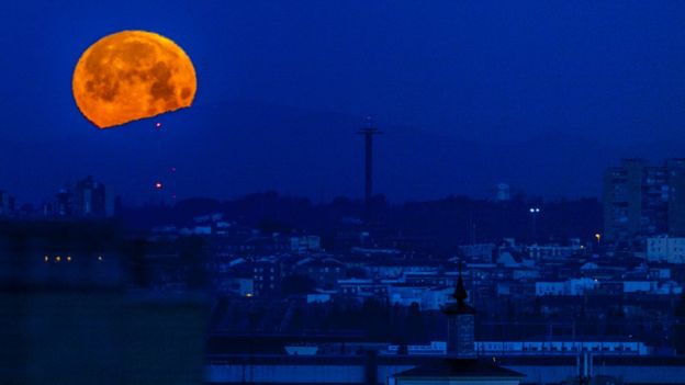 The bright orange moon set against a deep blue cityscape of Madrid, Spain