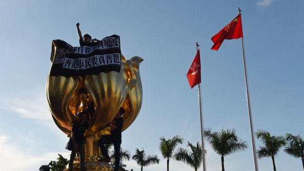 Activists on the monument given by China to Hong Kong in 1997