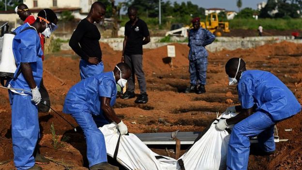 Health workers from the Sierra Leone's Red Cross Society Burial Team 7 place a body in a grave at King Tom cemetary in Freetown on November 12, 2014