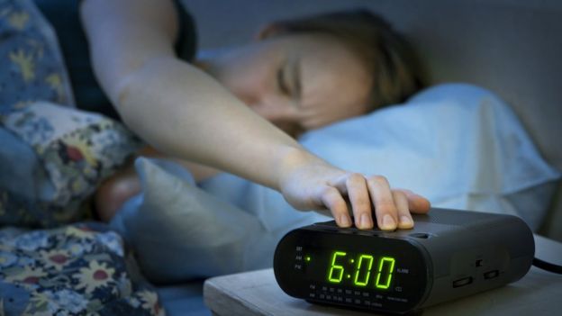 Una mujer cansada intenta apagar un despertador.