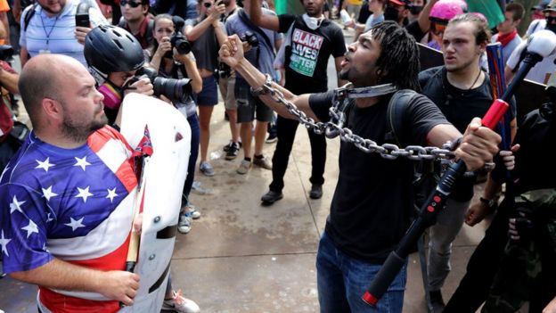 Un manifestante negro con cadenas se enfrenta a otro blanco con una camiseta de la bandera estadounidense