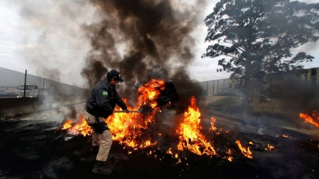 A member of the Federal Police removes a tire out of a burning barricade on BR-116 highway, during a protest against President Michel Temer in Sao Paulo, Brazil August 2, 2017.