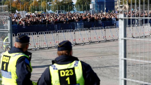 Police watch hundreds of people gathered behind barriers which keep part of the street clear