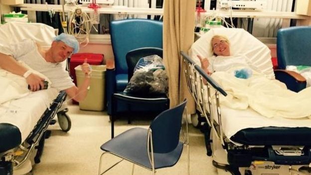 The couple each raise their thumbs from their hospital beds