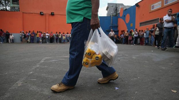 Hombre con compras en la mano y largas filas.