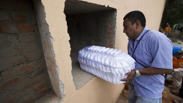 A relative places a five-month old baby Alezandro Macario into a tomb at the Santa Catarina Pinula cemetery on the outskirts of Guatemala City, Saturday, Oct. 3, 2015, after a fatal mudslide