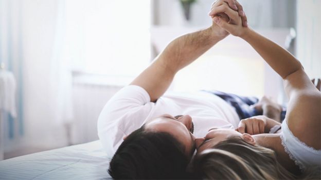 Una pareja acostada en una cama sujetándose las manos.