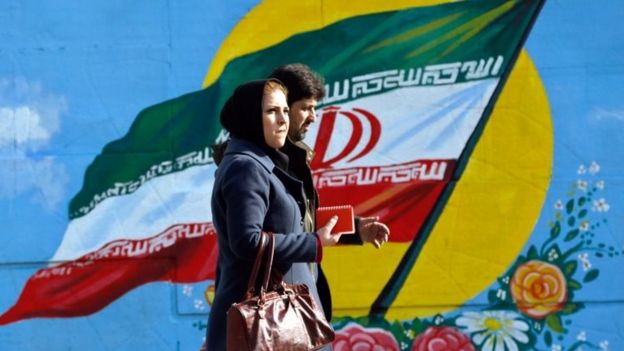 Iranians walk in front of a painting of Iran's national flag in Tehran. File photo