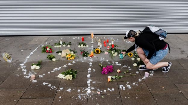 A woman places a candle at a makeshift memorial arranged like a peace sign at the scene of a knife attack in the northern German city of Hamburg, 29 July 2017