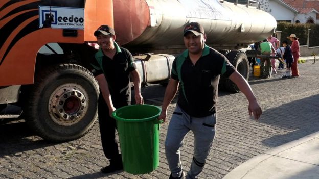 Dos personas cargan una gran cubeta de agua.