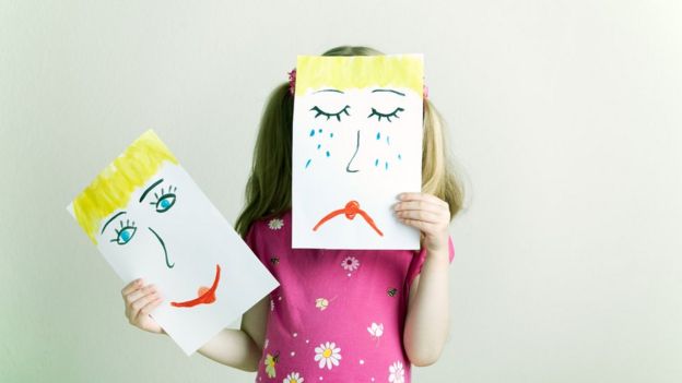 Criança segura desenhos simbolizando tristeza e alegria