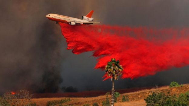 A DC-10 aircraft drops fire retardant on a wind driven wildfire in Orange, California