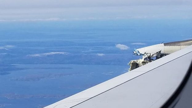 A view over the wing, showing land in the distance beyond, while the plane is still airborne. Mangled metal can be seen poking above the surface.