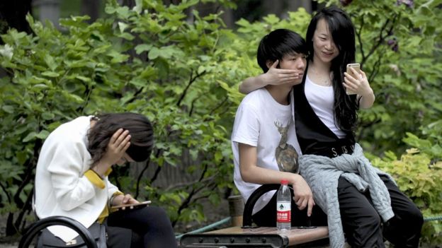 A couple use a mobile phone to take a picture at a park in Beijing