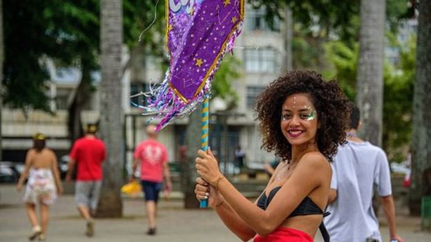 Mulher com glitter no rosto segura porta-estandarte no Carnaval