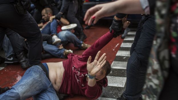 A man lying on the floor is dragged away by one arm, by a police officer.