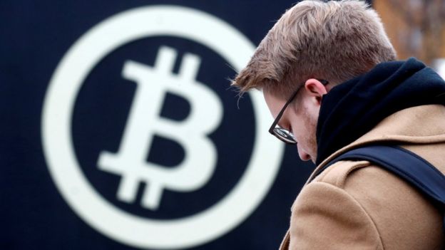 Um homem em frente ao logo da bitcoin